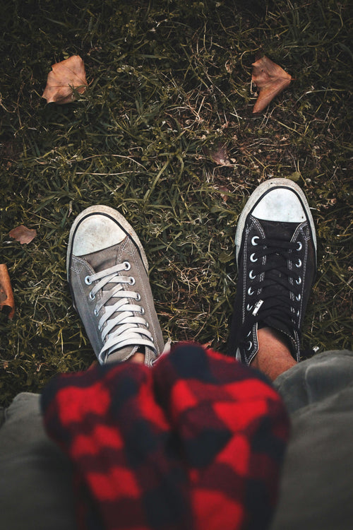 Top-down view of a person wearing mismatched sneakers  one black, one grey standing on grass with a red plaid shirt